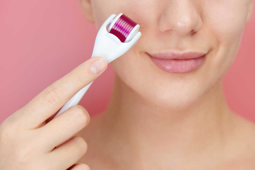 Close-up female face with dermaroller for mesotherapy procedures, skin care at home and in salon. Meso roller with microneedles on pink background